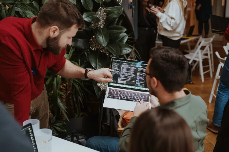 Člen týmu Aibility ukazuje druhému kolegovi kód na MacBooku — denní práce, AI jako první ruka